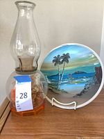 Full view of glass hurricane lamp and hand-painted plate on stand
