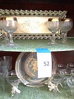Tray with metal leaf frame and four frosted gold-rimmed goblets; lower shelf shows black anniversary plate and additional stemware