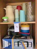 Shelf showing boxed Nissan vacuum bottle, black vacuum bottle, plastic cooler, ceramic coffee pot, glass vase and plastic tumblers