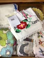 Drawer of assorted linens showing embroidered floral piece, tufted cloth, printed linens and number tag