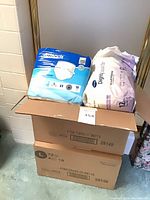 Open carton with Attends 18-count pack, Dignity 12-count pack, and sealed Attends 72-count case