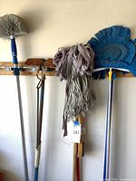 Group of cleaning tools hanging on wall showing various mop heads, dusters and handles