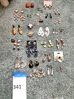Full layout of approximately 25 pairs of assorted earrings on carpet