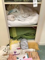 Closet shelf showing stacked white sheet and green blanket with various linens on floor