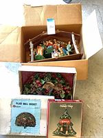 Open boxes showing nativity set in wooden stable, plaid wall basket wreath box and Holiday Harp Noël bell box