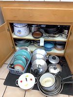 Cabinet with stacked cookware, showing enamel floral pot, stainless lids and fry pans