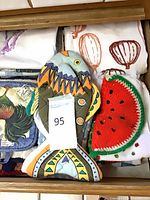 Top view of drawer containing fish-shaped oven mitt, crochet watermelon pot holder, rooster pot holder and several folded tea towels
