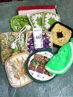 Assortment of crocheted and quilted potholders, mitts and trivets laid out to show colours, patterns and quantity