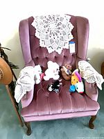 Front view of pink velvet wingback chair with antimacassar and plush toys on seat