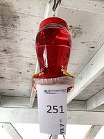 Entire hummingbird feeder hanging from hook showing red reservoir and yellow flower ports