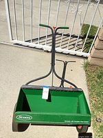 Full view of green Scotts push spreader in front of gate