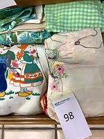 Folded aprons showing green gingham, children print and embroidered pieces