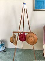 Full view of wooden easel with two straw hats and pink cap hanging