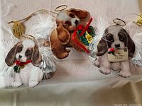Front view of three puppy angel ornaments with feather wings and gold hangers