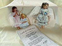 Front view of both angel ornaments on stand with certificate visible