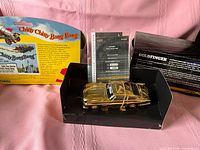 Rear view of boxed Chitty Chitty Bang Bang and gold Aston Martin in display case with booklet