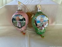 Front view of both Precious Moments ornaments showing colors, figurines, pictorial scenes and jewel drops