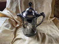 Front view of silver plated lidded jug showing engravings, handle and spout
