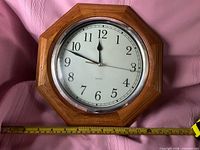 Front view showing wood frame, clock face and tape measure for size reference