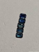 Five stacked emerald-cut blue sapphires on neutral background