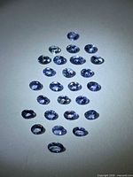 Group of approx 25 oval-cut tanzanites on white background