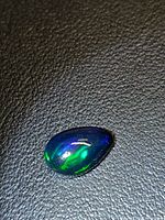 Pear cabochon opal showing blue and green flashes on dark background
