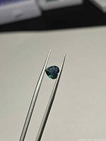 Front view of heart-cut blue-green sapphire held in tweezers