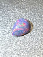 Pear-shape black opal cabochon showing bright color play under strong light
