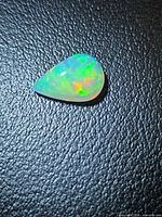 Pear cabochon opal showing play of colour on black background