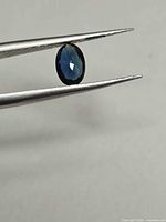Oval blue sapphire in tweezers showing face-up view