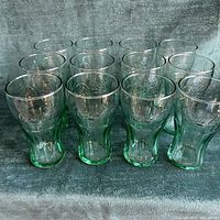 Front view of all 12 green-tinted Coca-Cola glasses arranged in rows