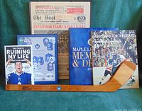 Group shot showing stick, three books, framed newspaper cover and jersey print