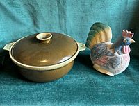 Casserole with lid and wooden rooster figure side by side