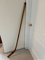 Full view of wooden hockey stick leaning against wall showing overall length and shape