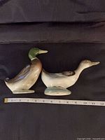 Both ceramic duck figurines side by side with tape for scale