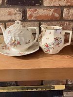 Front view of teapot, creamer and plate showing floral pattern