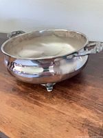 Angled side view showing one ornate handle and two of the four feet