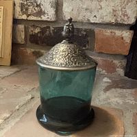Full view of green glass jar with ornate silver-plated lid in place