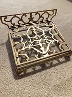 Top view of ornate brass book stand showing open-work pattern and folding shelf