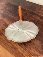 Top view of silver plate crumb catcher showing scalloped pan and orange handle