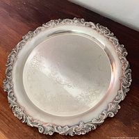Top view of round silver-plated tray showing engraved center and ornate border