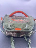Front view of Ugly Stik camouflage tackle bag showing brand logo, handle, rod tube holders and straps