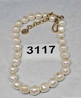 Necklace laid out showing faux pearls, gold-tone clasp, extender chain and Givenchy logo charm beside lot tag 3117
