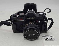 Front view of Konica Autoreflex camera with lens, cap and strap visible