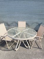 Round glass patio table with three chairs arranged outdoors
