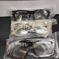 Three pairs of packaged reading glasses showing frame colors and +1.00 stickers