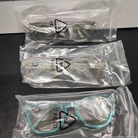 Three sealed pairs of reading glasses in grey, clear and teal