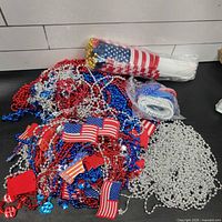 Pile of red, blue, silver bead necklaces, small rectangular flag pieces visible