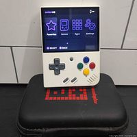 Front view of Anbernic RG35XX powered on, resting on black carry case