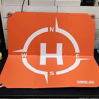 Orange side of STARTRC drone landing pad showing compass rose and H symbol